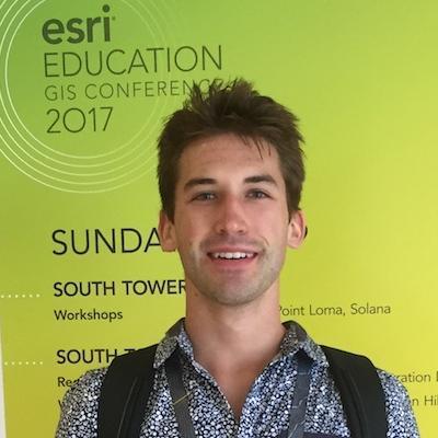 A person standing indoors, wearing a badge and lanyard, with a bright green backdrop. image link to story