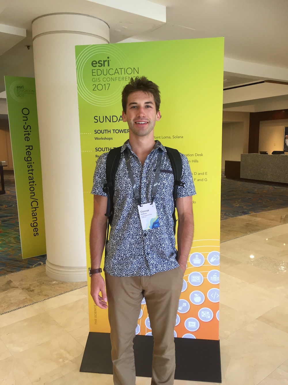 A person standing indoors, wearing a badge and lanyard, with a bright green backdrop. image link to story