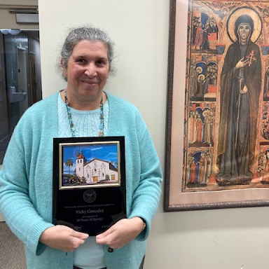 Vicky Gonzalez standing with her plaque next to religious painting