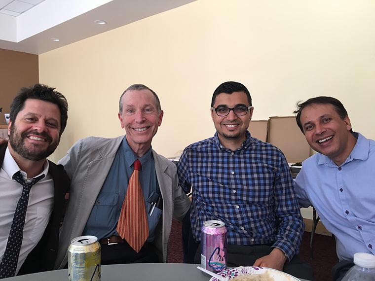 Four men smiling and sitting at a table with drinks.