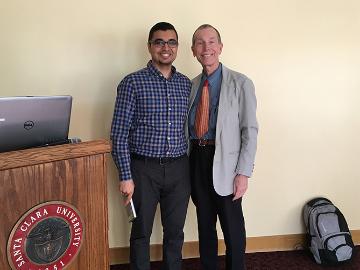 Two people standing near a podium with a laptop.