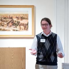 Person standing in front of a framed artwork, engaging in discussion or presentation.