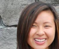 A woman smiles in front of a stone wall.