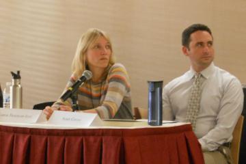 Two individuals sitting at a conference table with name placards. image link to story