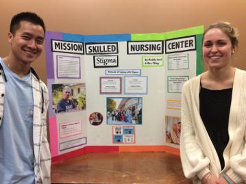 Two people standing in front of a project display board titled 