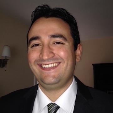 A person wearing a suit and tie, smiling.