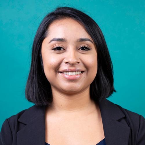 A smiling person in formal attire against a teal background. image link to story