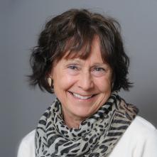 A woman smiling, wearing a patterned scarf and white top. image link to story