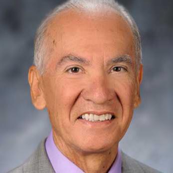 Alt text: Man in a suit smiling against a blurred background. image link to story