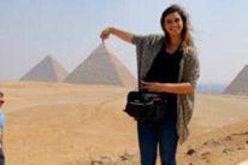 A person posing in front of pyramids, playfully holding one in perspective.