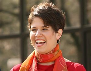 Person smiling and wearing red top and orange scarf outdoors. image link to story