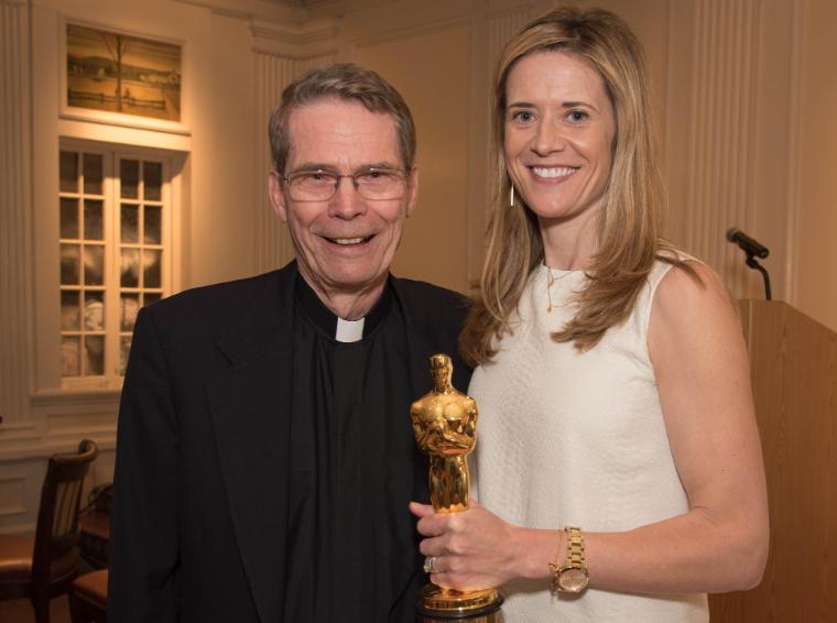 A woman holding a trophy stands next to a man in clerical attire. image link to story