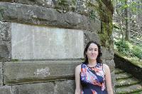 Woman standing beside ancient stone wall in a wooded area. image link to story