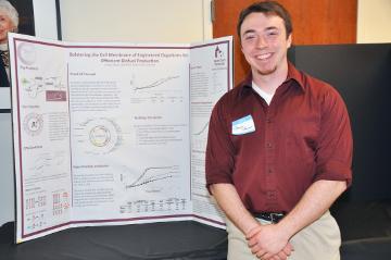 A person stands next to a presentation poster. image link to story