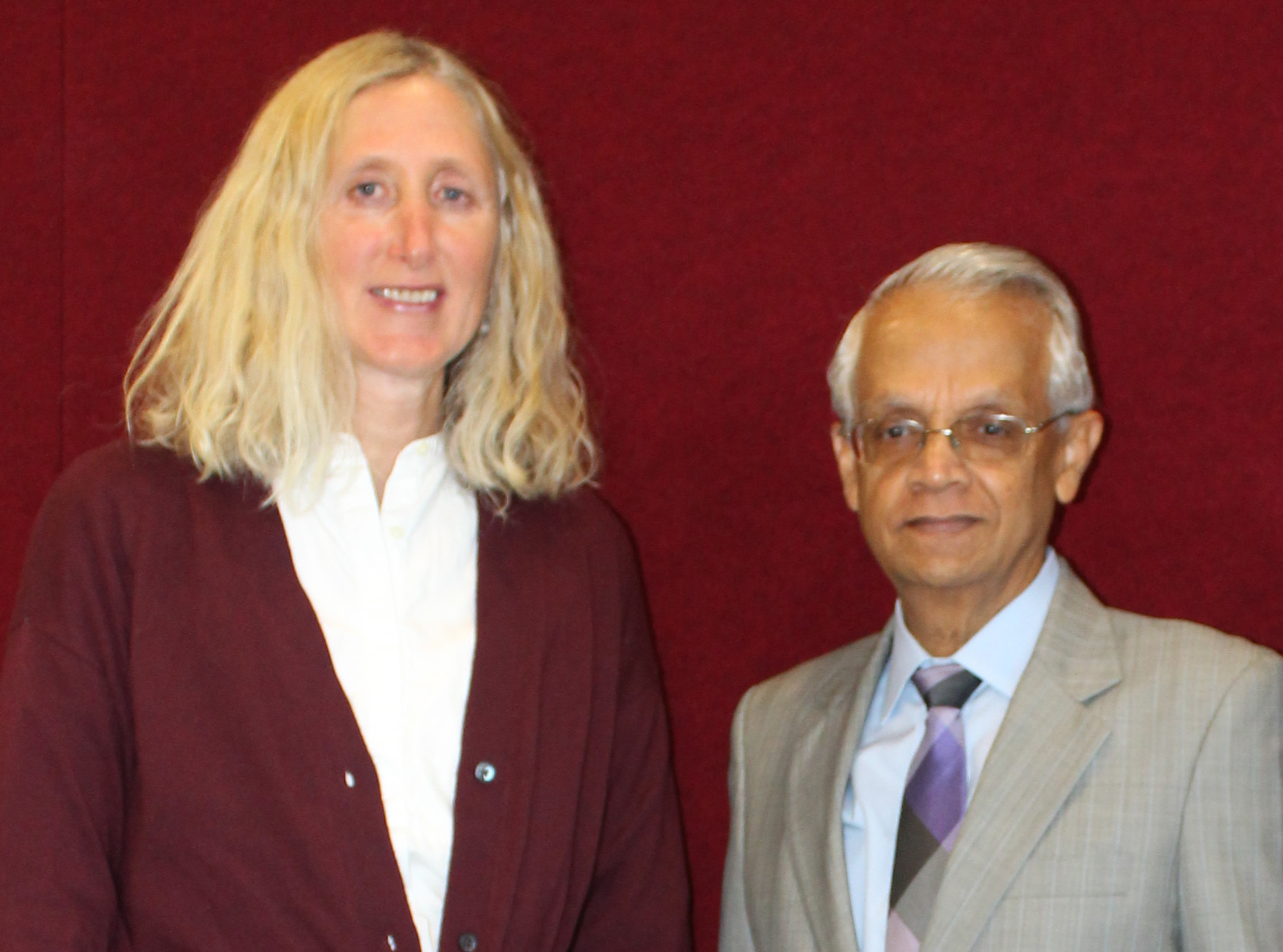 Two people standing together in front of a red background. image link to story