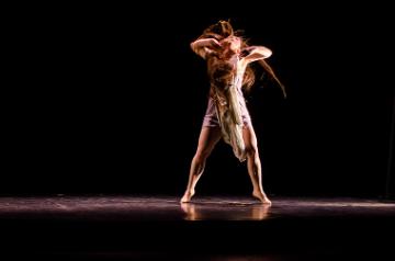 A person dancing on stage under dramatic lighting.