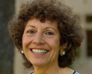 A woman smiling, wearing a light blue top and earrings. image link to story