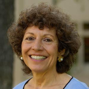 A woman smiling, wearing a light blue top and earrings.