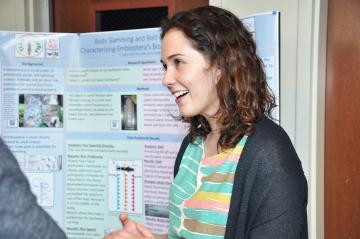 A woman smiles in front of a scientific poster. image link to story