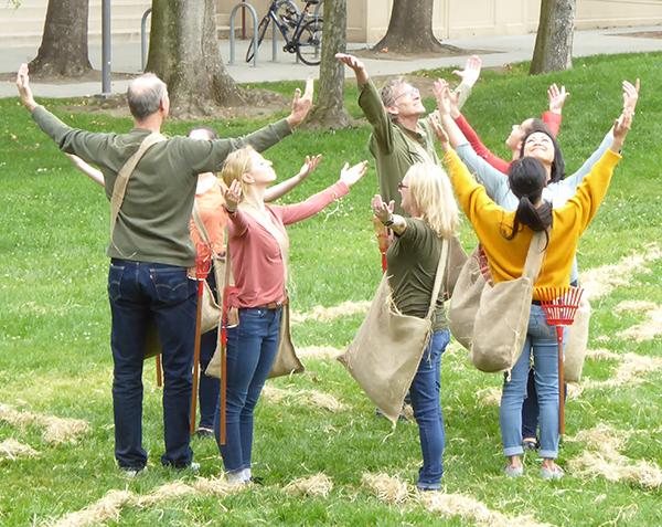 Group of people with their arms outstretch upwards and their faces facing towards the sky with hay scattered around them