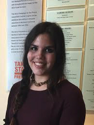 A smiling person standing in front of bulletin boards.