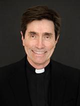A person wearing clerical clothing and a white collar, smiling against a black background. image link to story