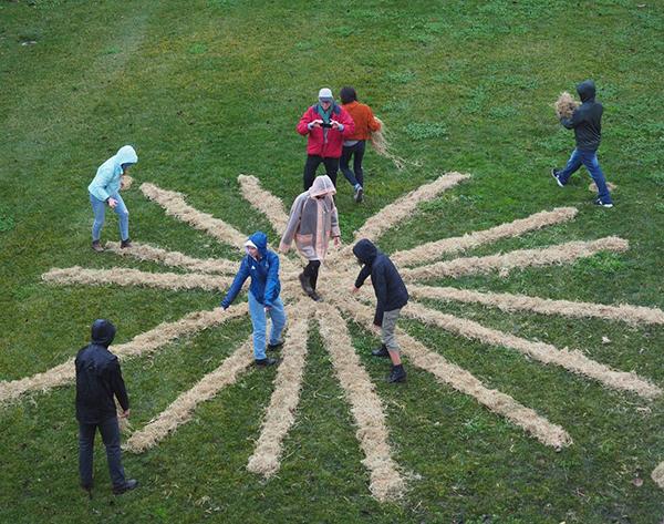 People arranging dry hay on grass in an asterisk type shape