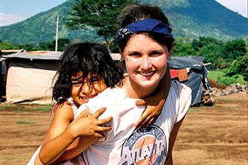 Woman carrying a young child with mountains in the background. image link to story