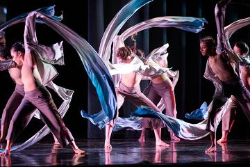 Dancers swirling white silk scarves around their bodies lit with blue light