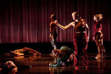 4 female dance students on stage wearing burgundy tops and brown pants in front of a red curtain