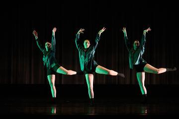 3 female dancers in bright green shirts and black shorts onstage with their hands lifted and