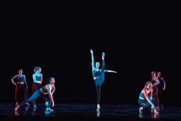 Female dancer in high kick flanked by 2 dancers on their knees