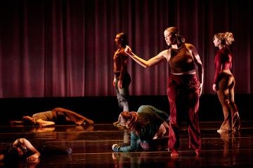 4 female dance students on stage wearing burgundy tops and brown pants in front of a red curtain
