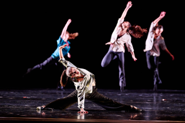 A female dancer sliding into the splits with 3 women behind her with their arms in the air