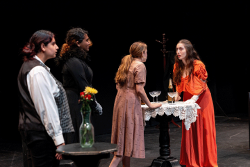4 women standing at a tall round table arguing