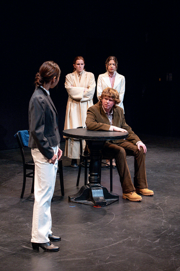 A man seated at a round table arguing with 3 women standing aound him
