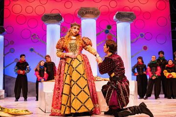 A kin in a burgundy velvet suit kneeling in front of a queen in an Elizabethan dress