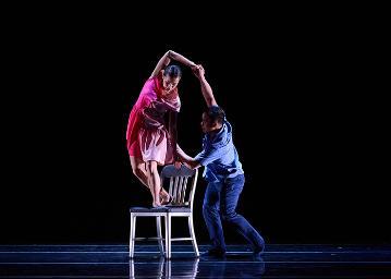 A man in blue lifting a woman in pink over the back of a white wooden chair