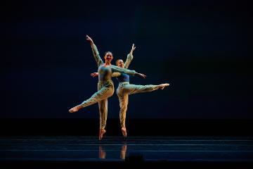 2 female dancers in teal leotards and leggings in split jumps