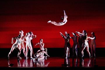 A female dancer in white onstage flying from a group on the left to a group on the right