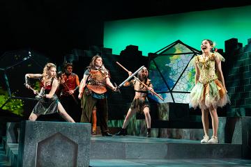 A fairy on a fantastical stage with 3 female D&D questers and a man dressed as the devil
