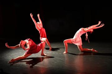 3 female dancers in red dresses kneeling and leaning back with their arms overhead