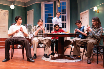 5 men seated at a table playing cards with a 6th man standing behind them