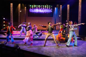 Students dancing onstage wearing 1970s clothes