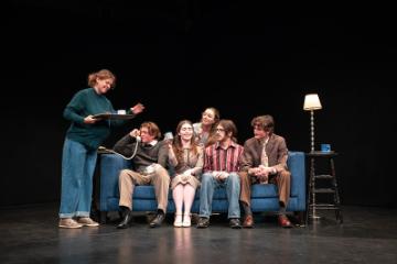 5 people squished on a blue couch, one talking on a rotary phone, looking at a woman bringing coffee on a tray