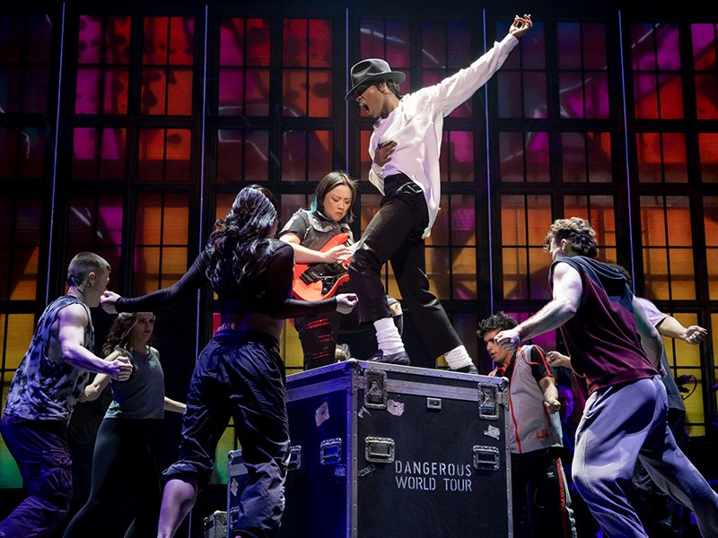 A performance of MJ at The Tonys. The actor playing Michael Jackson is standing on top of a black box as six other performers stand around the box.
