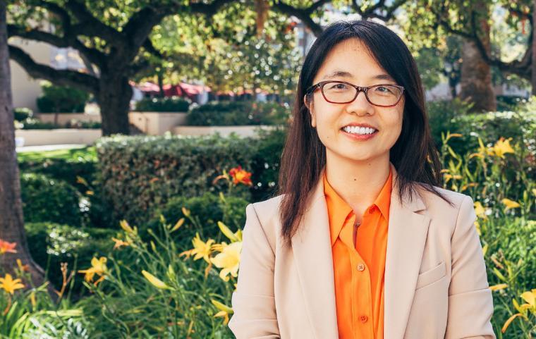 Yuhong Liu smiling in a beige suit with an orange top. 