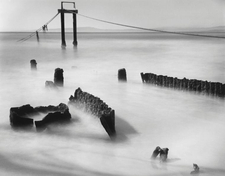 Black and white photograph of pylons emerging from fog. Shot from ground level.