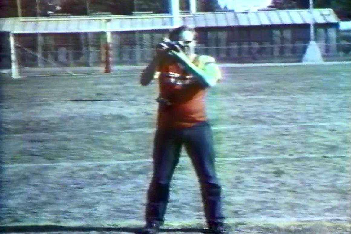Film still of man in red t-shirt looking through the viewfinder of a camera.