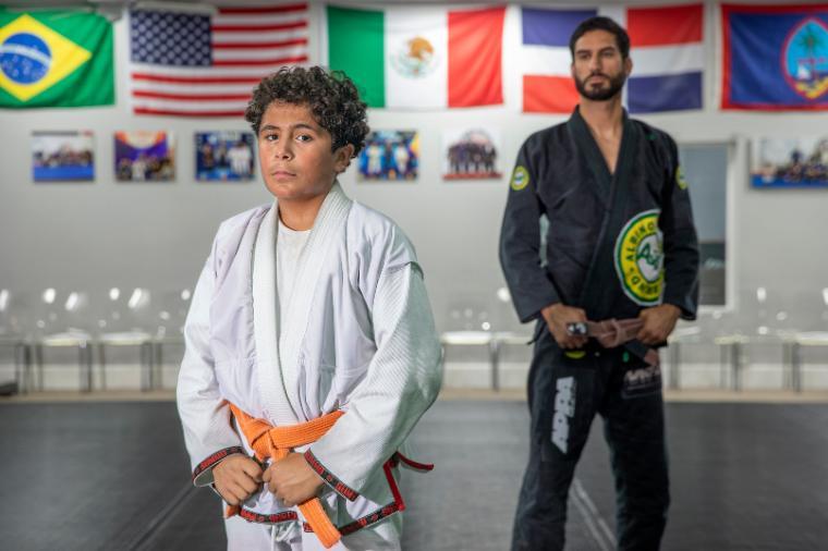 young boy standing in white martial arts attire and man in black martial arts attire in background
